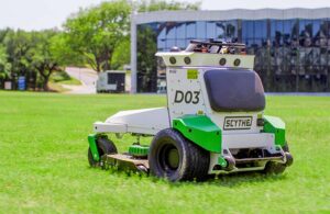 scythe robotics autonomous mower on the grass in front of a commercial building.
